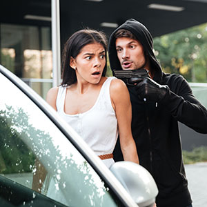 Armed Robbery: A masked man in a black hoodie pointing a handgun at a startled woman sitting in her car.