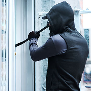 Burglary: A masked individual using a crowbar to pry open a glass door of a building.