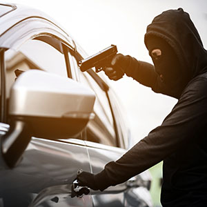 Carjacking: An armed individual in a mask pointing a gun at a car window to seize the vehicle.
