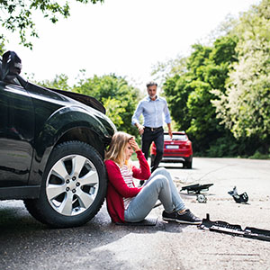 Hit & Run: A woman sitting on the ground next to a damaged black car after an accident.