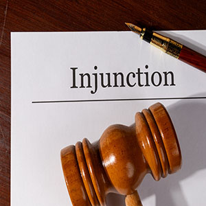 Injunctions: A wooden legal gavel and a fountain pen resting on an "Injunction" document.