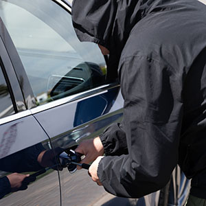 Theft Crimes: A person in a black hoodie attempting to break into a car door using a tool.