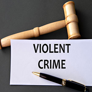 Violent Crimes: A wooden legal gavel resting on a white card that reads "VIOLENT CRIME" next to a fountain pen.
