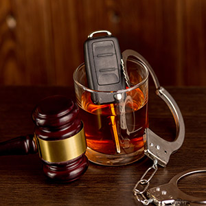 Car keys inside a glass of whiskey next to handcuffs and a judge's gavel: common DUI defense strategies.