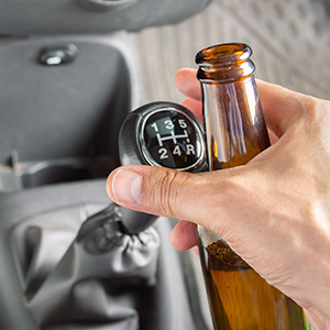 Hand holding a beer bottle inside a vehicle, highlighting the dangers of drinking and driving