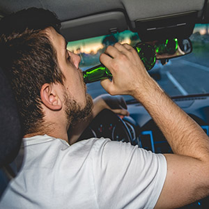 Young man drinking from a bottle inside a car, highlighting the risks of holiday drunk driving.