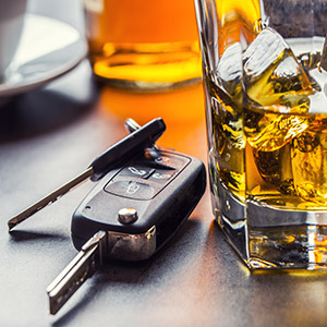 Car keys next to a glass of alcohol on a table, symbolizing the impact of a DUI on insurance premiums.