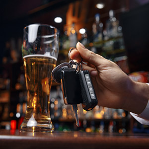 Close-up of a person holding car keys next to a glass of beer at a bar, symbolizing DUI risks during Labor Day.