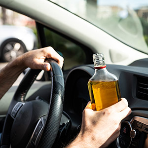 Person driving a car while holding a bottle of liquor, illustrating criminal offenses and potential 10-20-Life charges.