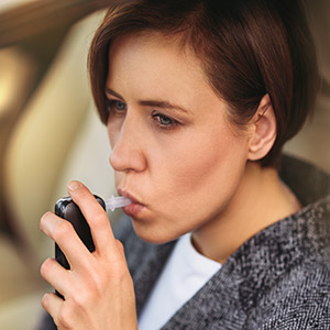 Distressed woman blowing into a breathalyzer machine for a DUI chemical test.