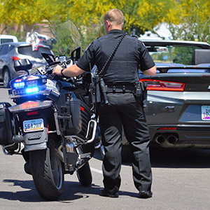 Police officer standing next to a motorcycle during a traffic stop on a highway.