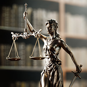 Lady Justice statue holding scales and a sword in front of a law library bookshelf.