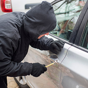 Person in a hoodie using a tool to break into a car door: legal defense for theft crimes.