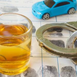 Handcuffs, a blue toy car, and a glass of alcohol illustrating DUI and traffic law concepts.